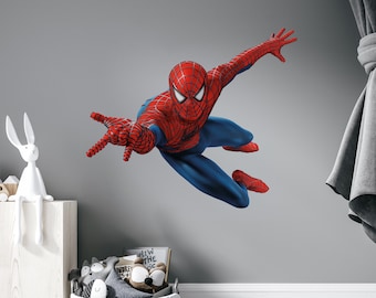May include: A red and blue Spider-Man wall decal in a child's bedroom. The decal shows Spider-Man in mid-air, reaching out with his left hand. The decal is on a gray wall, and there is a white toy rabbit on a shelf to the left of the decal.
