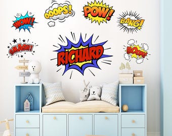 May include: Comic book-style wall decals with phrases like "WOW!", "POW!", and "SMASH!" in bold, colorful fonts. A large decal spells out "RICHARD". The decals are displayed above a light blue storage unit with a bench cushion.