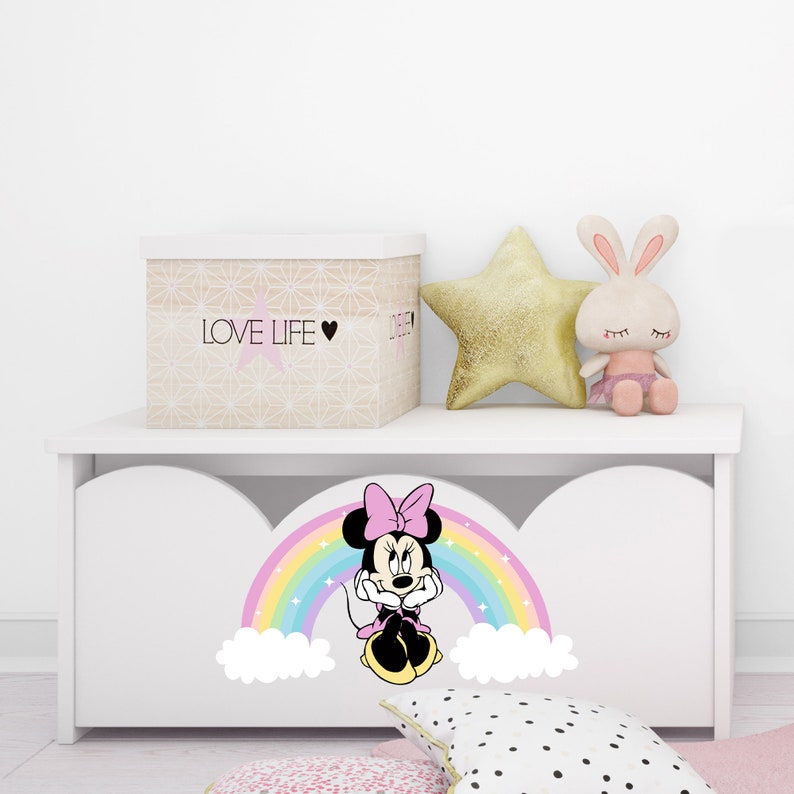 Pode incluir: Ba&uacute; de armazenamento de brinquedos branco com um arco-&iacute;ris e um design de Minnie Mouse. O ba&uacute; tem uma borda festoneada e uma tampa branca. Uma caixa rosa com as palavras "LOVE LIFE" est&aacute; em cima do ba&uacute;.