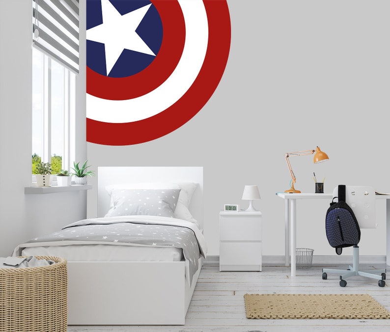 May include: A white twin-sized bed with a gray and white patterned comforter and a white headboard. A red, white, and blue half-circle Captain America shield decal is on the wall behind the bed.