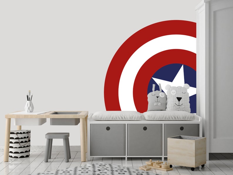 May include: A white, gray, and wood children's desk and bench set with a red, white, and blue Captain America shield decal on the wall behind it.