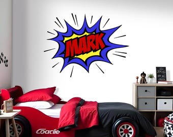 May include: A red race car bed with black and red bedding. The headboard features a comic book style burst with the name "MARK" in red letters. The bed has a low profile and a sporty design.