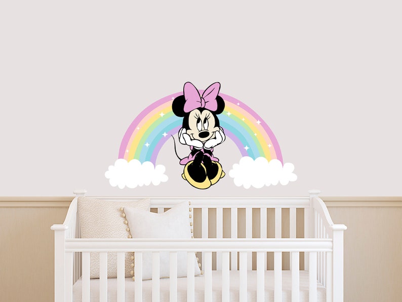 Pode incluir: Um ber&ccedil;o branco com um adesivo de parede Minnie Mouse rosa e arco-&iacute;ris. O adesivo apresenta Minnie Mouse sentada em um arco-&iacute;ris com nuvens de cada lado.