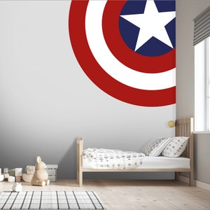 May include: A white, red, and blue Captain America shield decal on a gray wall in a child's bedroom. The decal is in the shape of a circle and has a white star in the center. The room also features a wooden bed with white bedding and a wooden nightstand.