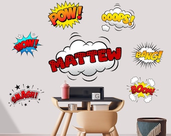 May include: Comic book-style wall art featuring speech bubbles with words like "POW!", "WOW!", and "SMASH!". The name "MATTEW" is displayed in a large speech bubble. A small desk with a red bottle and a black box is in the foreground.