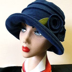 May include: A blue fleece cloche hat with a green leaf and three blue felt rosettes.