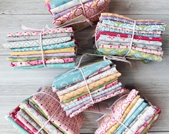 May include: Several bundles of patterned fabric in pastel colours, tied with white string. The fabric designs include floral and geometric patterns in pink, blue, yellow, and green. The bundles are arranged on a light wood surface.