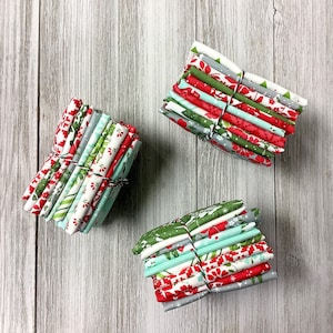 May include: Three stacks of folded fabric squares tied with thin twine. The fabric features various patterns in red, green, white, and light blue, including floral, geometric, and striped designs. Each stack contains multiple layers of cotton material.