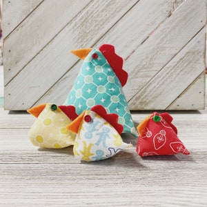 May include: Four handmade fabric chickens in various colors and patterns. The largest chicken is teal with white polka dots, the next largest is yellow with white polka dots, the next is white with blue and white gingerbread people, and the smallest is red with white lightbulbs.