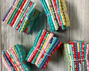 May include: A collection of ten fabric bundles, each containing multiple fabric strips. The bundles are arranged in a semi-circle on a white wooden surface. The fabric strips are a mix of red, blue, green, and white with floral and geometric patterns.