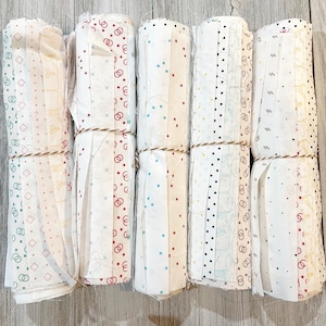 May include: Five rolls of white fabric with different patterns, including circles, dots, and lines. The fabric is tied with twine and is ready for quilting or other crafting projects.