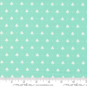 May include: A close-up of a fabric with a repeating pattern of white Christmas trees on a light teal background. The fabric has a ruler along the bottom edge with the word "moda" printed on it.