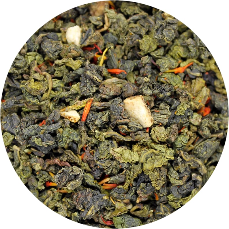 May include: Close-up of a blend of green tea leaves, dried orange peel, and other herbs. The tea leaves are a dark green color and the orange peel is a bright orange color.