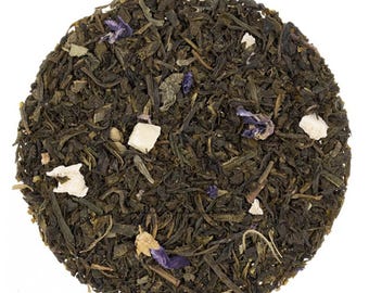 May include: A close-up of a blend of green tea leaves, white pieces of fruit, and purple flower petals.