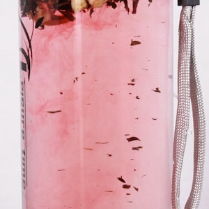 May include: A clear plastic bottle with a gray carrying strap. The bottle is filled with a pink liquid and contains dried fruit and herbs. The bottle has the text "Leisure Time" printed on the side.