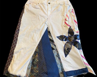 May include: A white denim skirt with a patchwork design. The skirt is made from different fabrics, including blue and white patterned ties, and has a large flower design on the front.