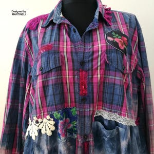 Puede incluir: Una camisa a cuadros patchwork en azul y rosa, con parches florales, ribetes de encaje y detalles de lentejuelas. La camisa tiene cuello y bolsillos de mezclilla, con el texto "Designed by MARTINELI" visible.