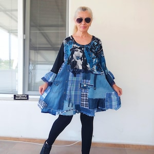 May include: A patchwork denim dress with a graphic print of a woman with a lollipop. The dress combines blue denim and plaid fabrics, with long black sleeves and a flared skirt. The text "Designed by MARTINELI" is visible.