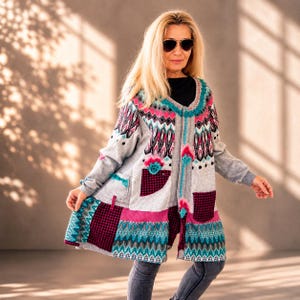 Könnte beinhalten: Eine langärmelige Strickjacke mit Patchwork-Design in Grau, Pink, Schwarz und Türkis mit geometrischen Mustern. Das Kleidungsstück verfügt über einen Rundhalsausschnitt, zwei Vordertaschen mit schwarz-weißem Hahnentrittmuster und eine Knopfleiste.