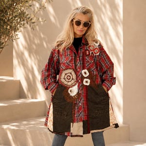 Puede incluir: Una camisa de manga larga con botones, con un patrón de cuadros rojos y negros, acentuada con paneles de mezclilla marrón oscuro en la parte inferior frontal, aplicaciones de ganchillo circulares en blanco y rojo, y un borde estampado.