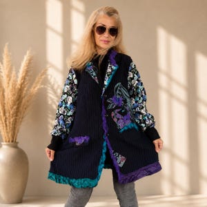 Può includere: Un cappotto a righe blu navy con maniche floreali e dettagli viola e turchese. Il cappotto presenta un design patchwork unico con motivi floreali e geometrici. Il cappotto ha un orlo a balze e una chiusura con bottoni. Le maniche sono nere con motivi floreali.