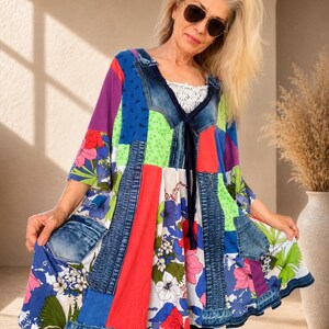 Puede incluir: Vestido túnica patchwork con paneles de mezclilla, florales y de tela lisa en azul, rojo, morado y verde. El vestido tiene cuello en V con una inserción de encaje blanco y una corbata azul oscuro. Las mangas son tres cuartos.