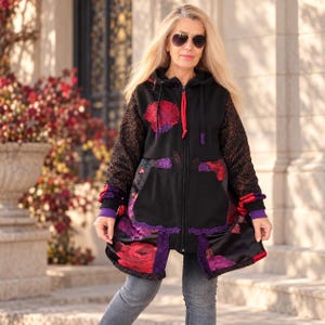 Puede incluir: Una sudadera negra con cremallera, mangas largas con patrón texturizado oscuro, capucha con cordones rojos y un estampado floral vibrante en tonos rojos y morados en los paneles frontales y el dobladillo. Incluye un bolsillo tipo canguro.