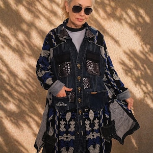 Può includere: Giacca di jeans lunga con design patchwork. La giacca presenta tessuto a fantasia blu, nero e grigio, dettagli di paillettes e chiusure con bottoni. Le maniche e i pannelli inferiori hanno motivi unici, creando un look elegante e a strati.