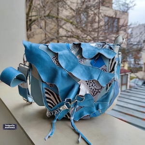 以下が含まれることがあります： ユニークなパッチワークデザインのライトブルーのクロスボディバッグ。ゼブラ柄や花柄など、さまざまなテクスチャとパターンが特徴です。ショルダー ストラップとフラップ開閉部が付いています。