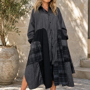 Può includere: Un abito camicia a maniche lunghe con un design patchwork nei toni del nero e del grigio antracite. Il capo incorpora diverse texture, tra cui sottili gessati, pannelli neri a tinta unita e un motivo a quadri scuri su tutto il tessuto.