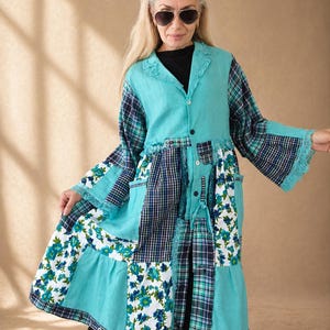 Peut inclure: Un manteau patchwork dans les tons turquoise, marine et blanc. Le manteau présente un mélange de panneaux de tissu floral, à carreaux et unis. Il a un col, une fermeture à boutons et des manches longues avec une bordure en dentelle. Le manteau arrive au genou.