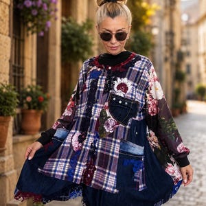 May include: A long-sleeved tunic featuring a patchwork design of blue and white plaid fabric, dark denim panels, and floral print sections. The garment includes a chest pocket, a button-down front, and decorative lace trim along the hem and seams.
