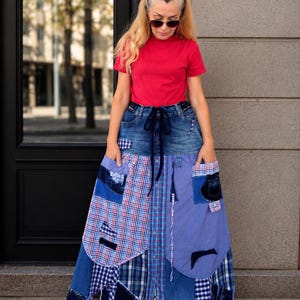 Könnte beinhalten: Ein leuchtend rotes Kurzarm-T-Shirt kombiniert mit einem langen Rock im Patchwork-Stil. Der Rock verfügt über einen dunkelblauen Jeansbund mit Kordelzug sowie verschiedene Stoffbahnen aus blau-weißem Karomuster und blauem Jeansstoff.