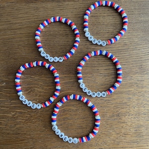 Può includere: Cinque braccialetti circolari realizzati con piccole perline di argilla piatte rosse, bianche e blu. Ogni braccialetto presenta perline con lettere bianche che compongono PHILA, 76ERS, MAXEY, LEBRON e SIXERS, alternate a piccoli distanziatori argentati.