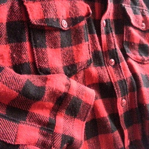 May include: Red and black plaid flannel shirt with a button-up front and two pockets.