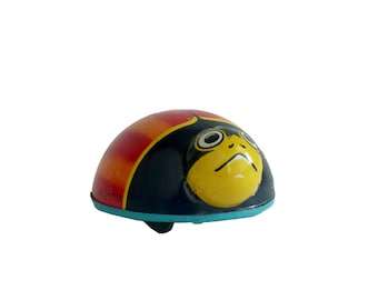 May include: A wind-up toy ladybug with a black, yellow, and red shell. The ladybug has a blue base and a black face with yellow eyes.