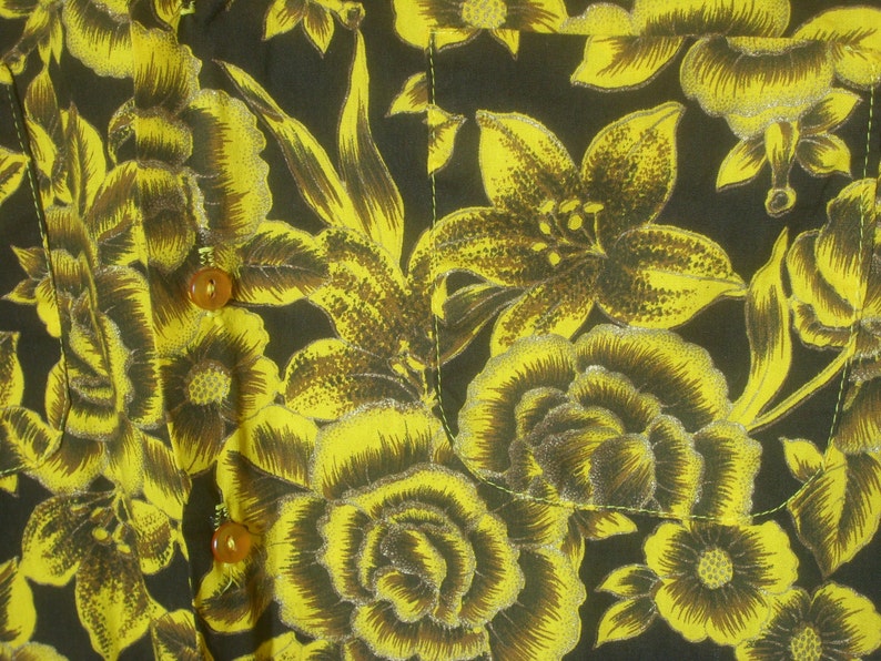 May include: A black fabric with a yellow floral pattern. The fabric has a shiny, almost metallic, finish. The flowers are lilies and roses.