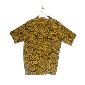 May include: A short-sleeved button-up shirt with a yellow floral pattern on a dark brown background.