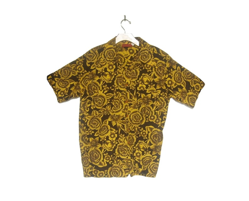May include: A short-sleeved button-up shirt with a yellow floral pattern on a dark brown background.