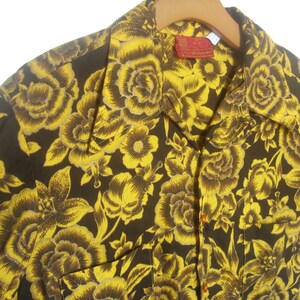 May include: A short-sleeved shirt with a brown background and a yellow floral pattern. The shirt has a collar and a button-up front.