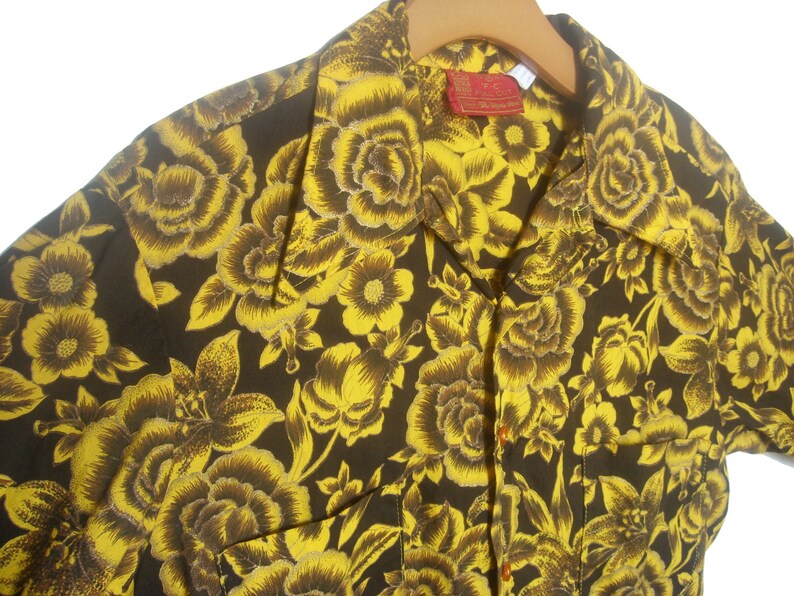 May include: A short-sleeved shirt with a brown background and a yellow floral pattern. The shirt has a collar and a button-up front.