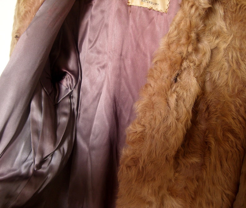May include: The inside of a brown fur coat with a satin lining. The lining is a light purple color. The label on the coat reads "Waterbury".