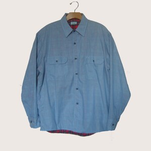 May include: A light blue long-sleeved button-down shirt with a plaid flannel lining. The shirt has two flap pockets on the chest.