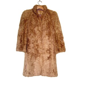May include: A brown faux fur coat with a collar and long sleeves. The coat is hanging on a wooden hanger.