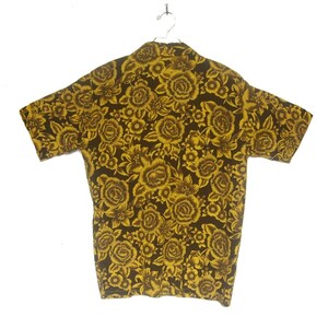 May include: A short-sleeved shirt with a brown background and a yellow floral pattern. The shirt has a collared neckline and a button-up front.