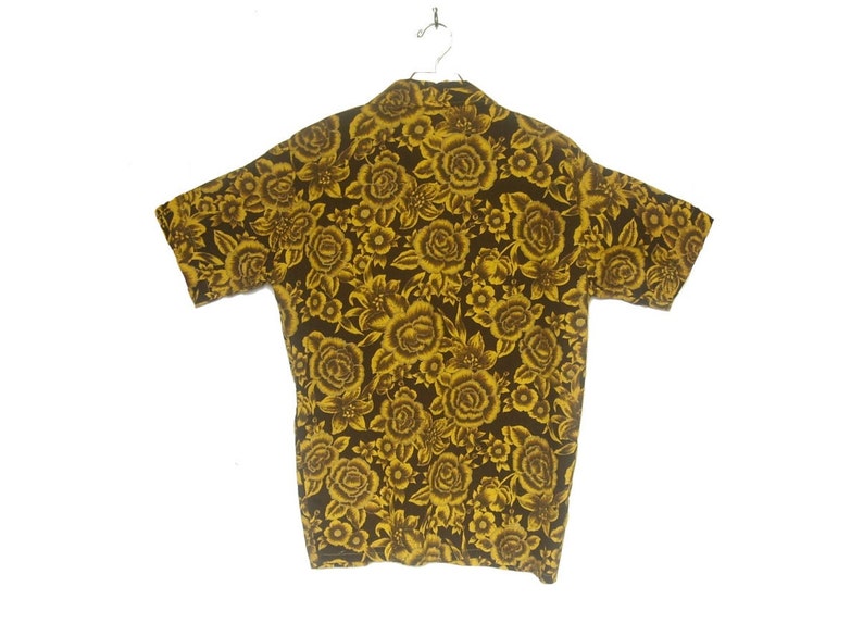 May include: A short-sleeved shirt with a brown background and a yellow floral pattern. The shirt has a collared neckline and a button-up front.
