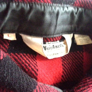 May include: Red and black plaid flannel shirt with a black collar and a white label that says "Woolrich" and "Clifan, Inc."
