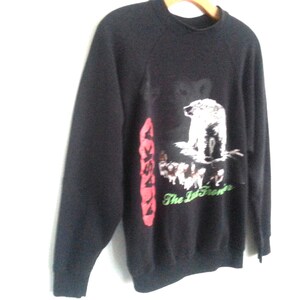 May include: Black sweatshirt with a graphic print of a polar bear and other animals. The text "Alaska The Last Frontier" is printed on the sweatshirt.