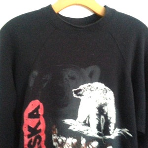 May include: Black sweatshirt with a white polar bear and the word "Alaska" in red on the front.