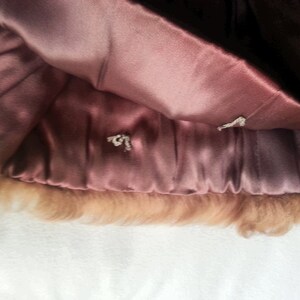 May include: A close-up of the inside of a brown fur coat. The lining is a soft, pink satin. The fur is a light brown color.